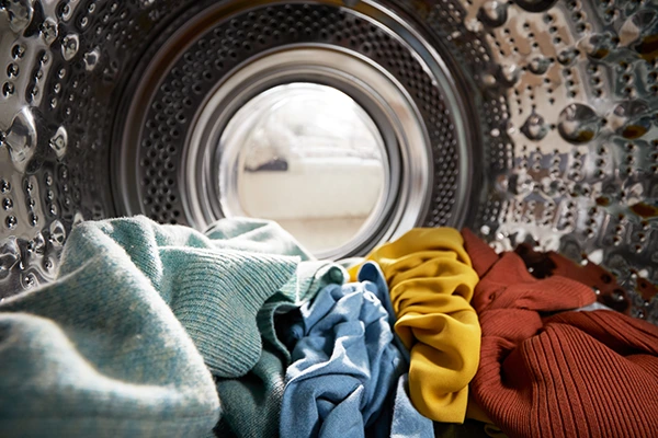 Inside a front-loading washing machine drum with colorful clothes piled at the bottom, viewed from the door opening.